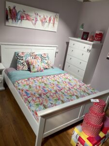 Dormitorio con colores vivos (azul, rosa, verde y naranja), hay una cómoda y cajas de color rojo de diferentes medidas colocadas una encima de la otra.