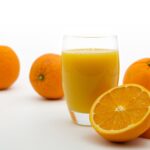Vaso transparente de cristal con zumo de naranja y hay naranjas a los lados.